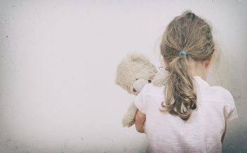 a little girls stands facing a wall holding a stuffed bunny